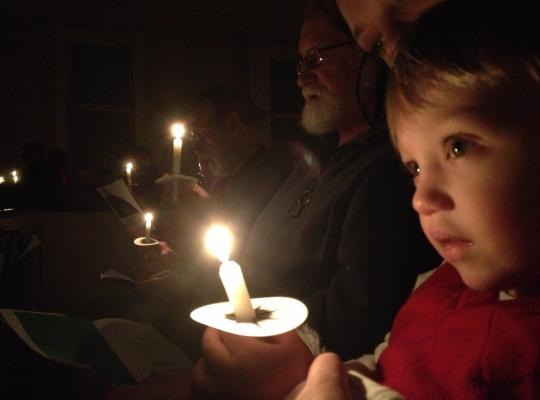 a child holds a candle at the Christmas Eve service